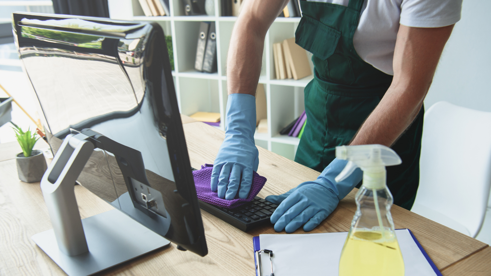 An office cleaner wiping down a computer keyboard.