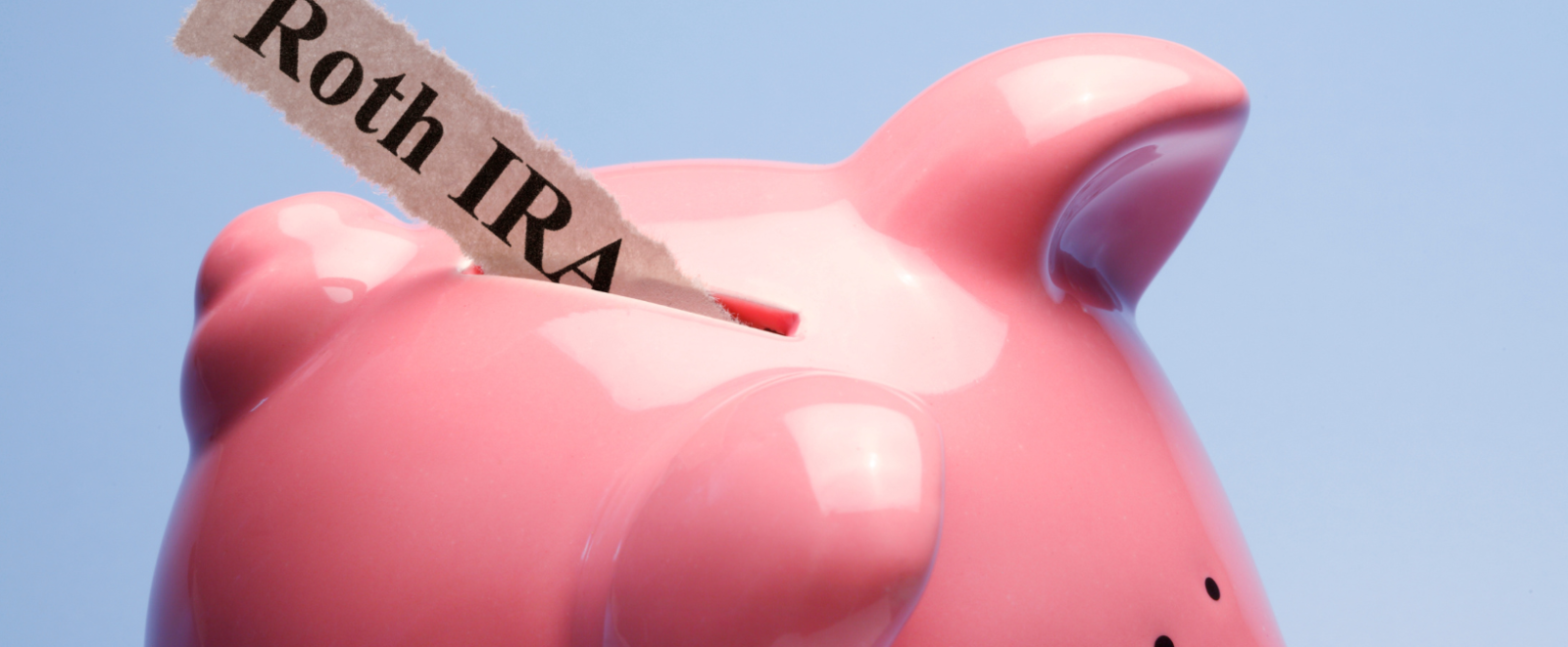 Paper labeled "Roth IRA" going into a piggy bank