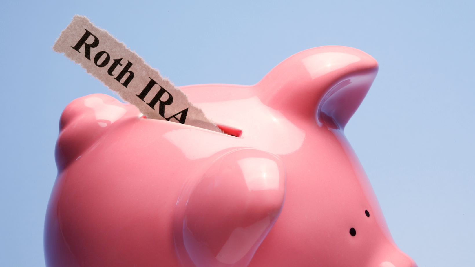 Paper labeled "Roth IRA" going into a piggy bank